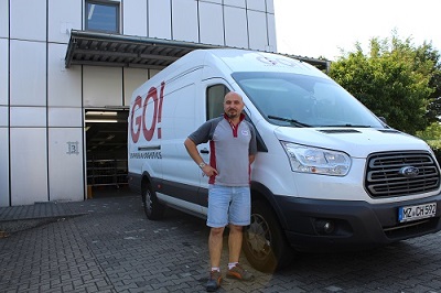 GO! Kurier steht vor einem GO! Transporter bereit seine Schicht zu starten

